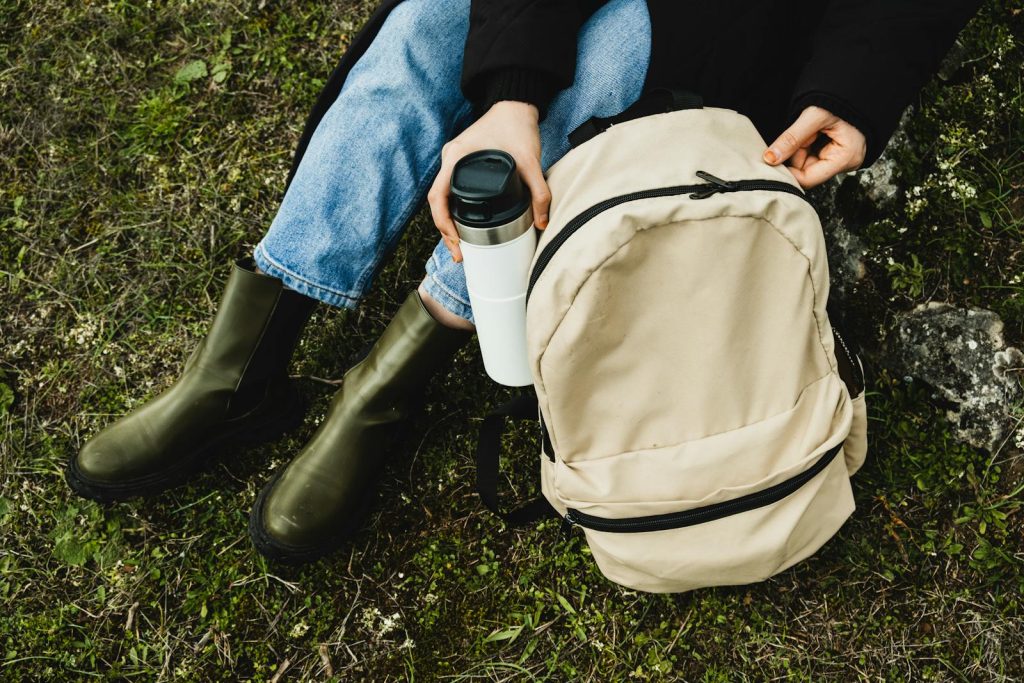 Person sitting outdoors with backpack and coffee cup, symbolizing adventure and relaxation.