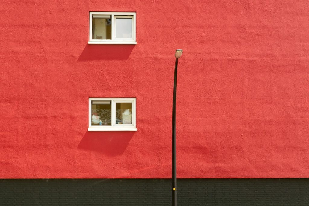 Minimalist urban scene with red wall, two windows, and street lamp.